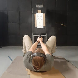 Student practicing defensive handgun shooting from a supine position during advanced CCW firearms training on a private range.