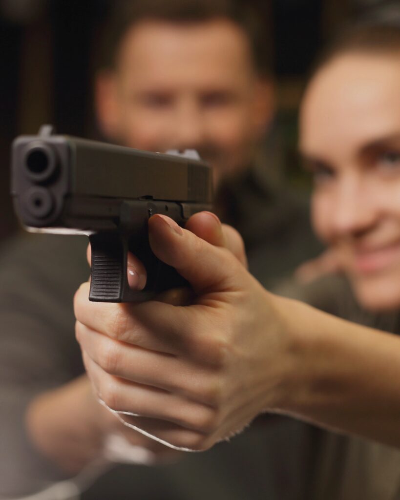 Female shooter practicing handgun fundamentals at an indoor range with a CCW-USA certified firearms instructor providing close supervision during live-fire training.