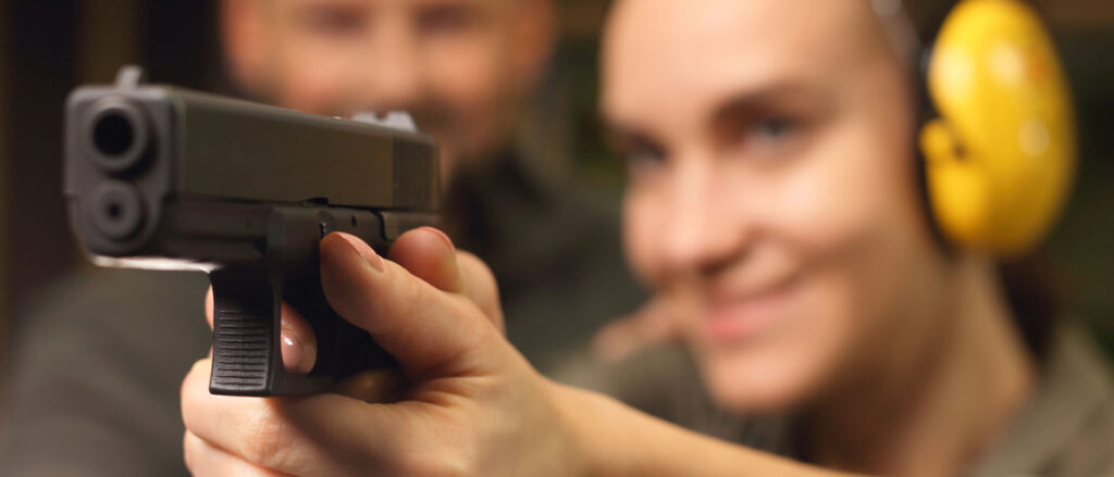 Female shooter practicing handgun fundamentals at an indoor range with a CCW-USA certified firearms instructor providing close supervision during live-fire training.